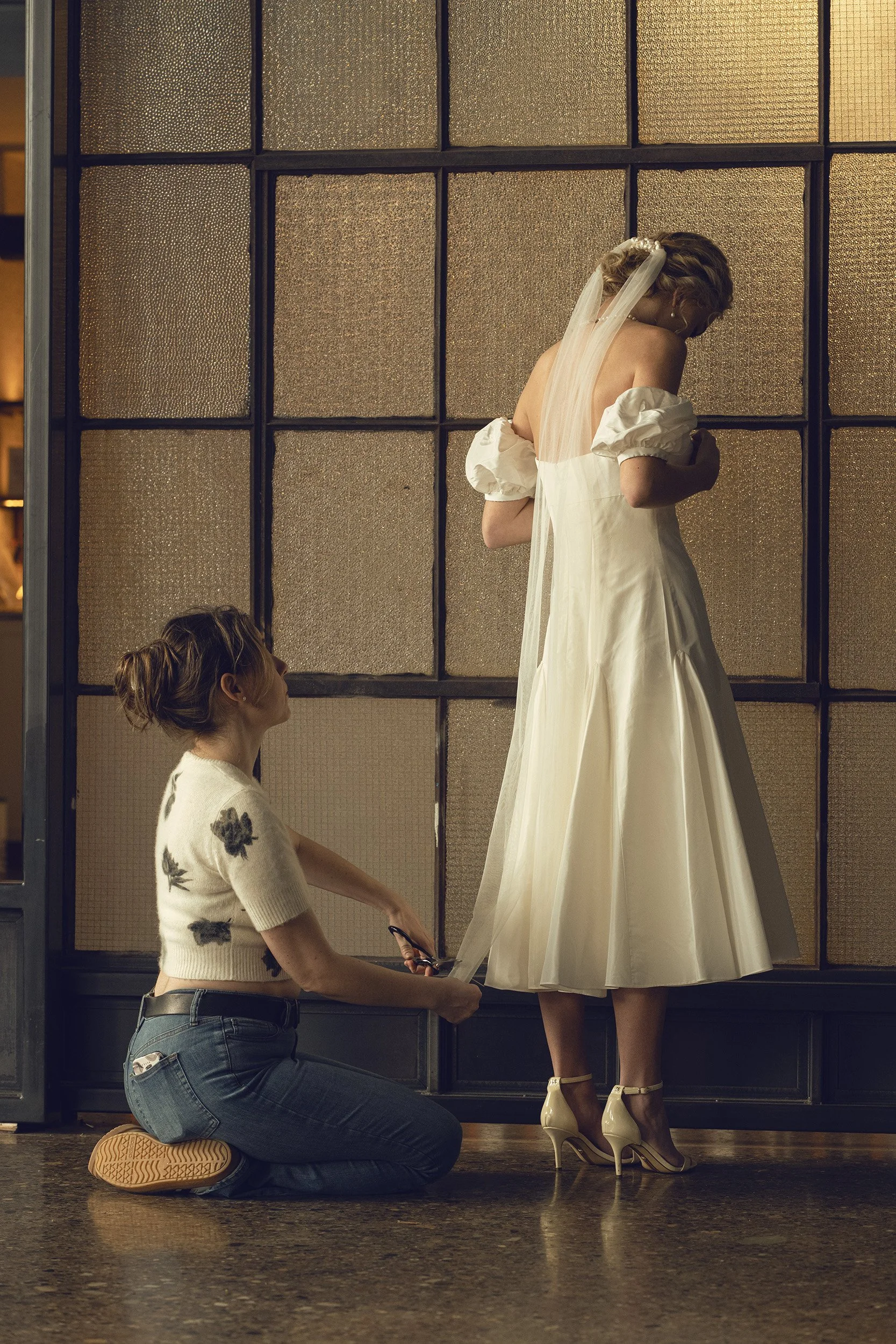 Custom couture fashion designer working with a bride wearing a tea length bridal gown and a pearl wedding veil.