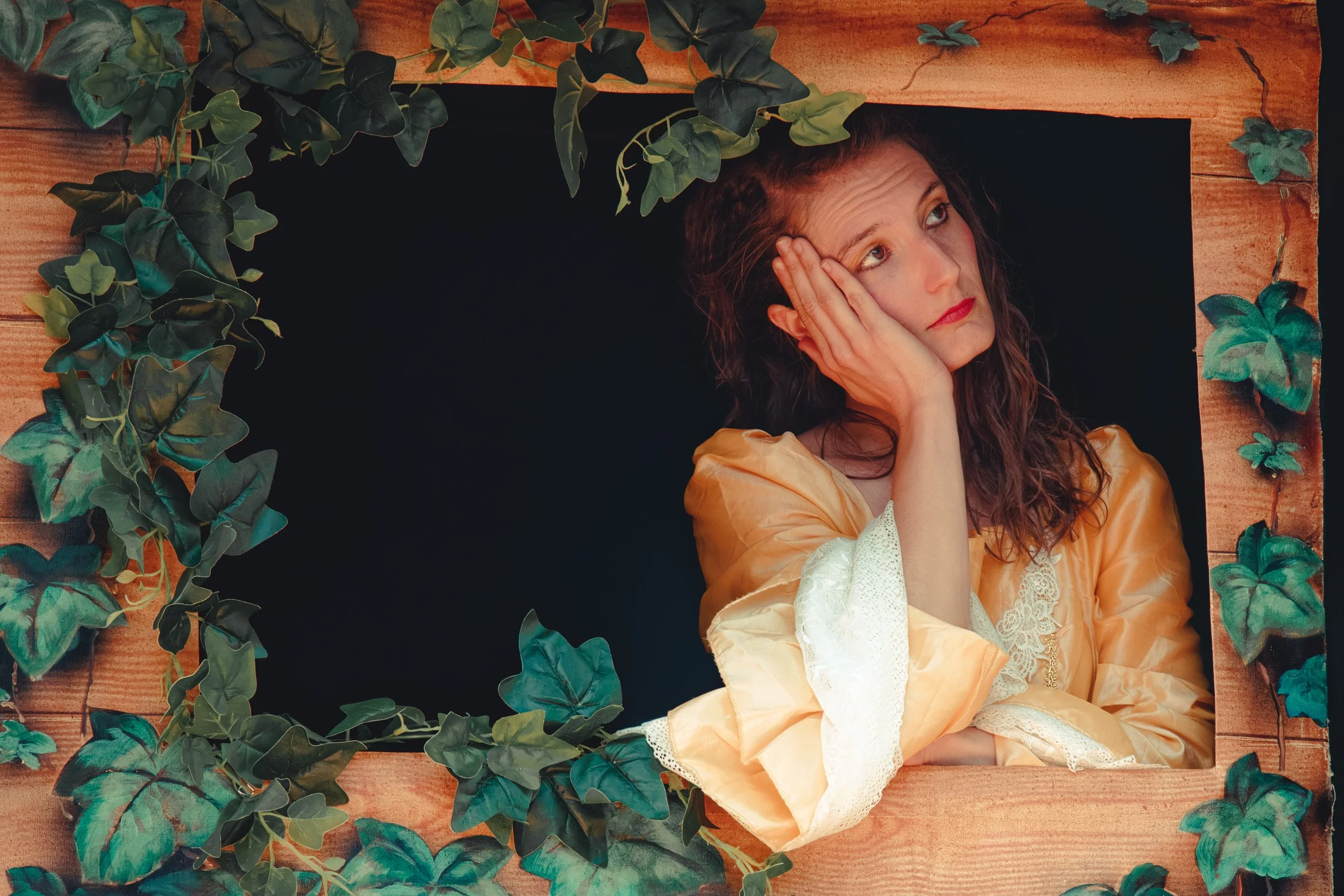 Une femme en robe jaune s'appuie sur sa main, l'air pensive, encadrée par une fenêtre rustique entourée de lierre.