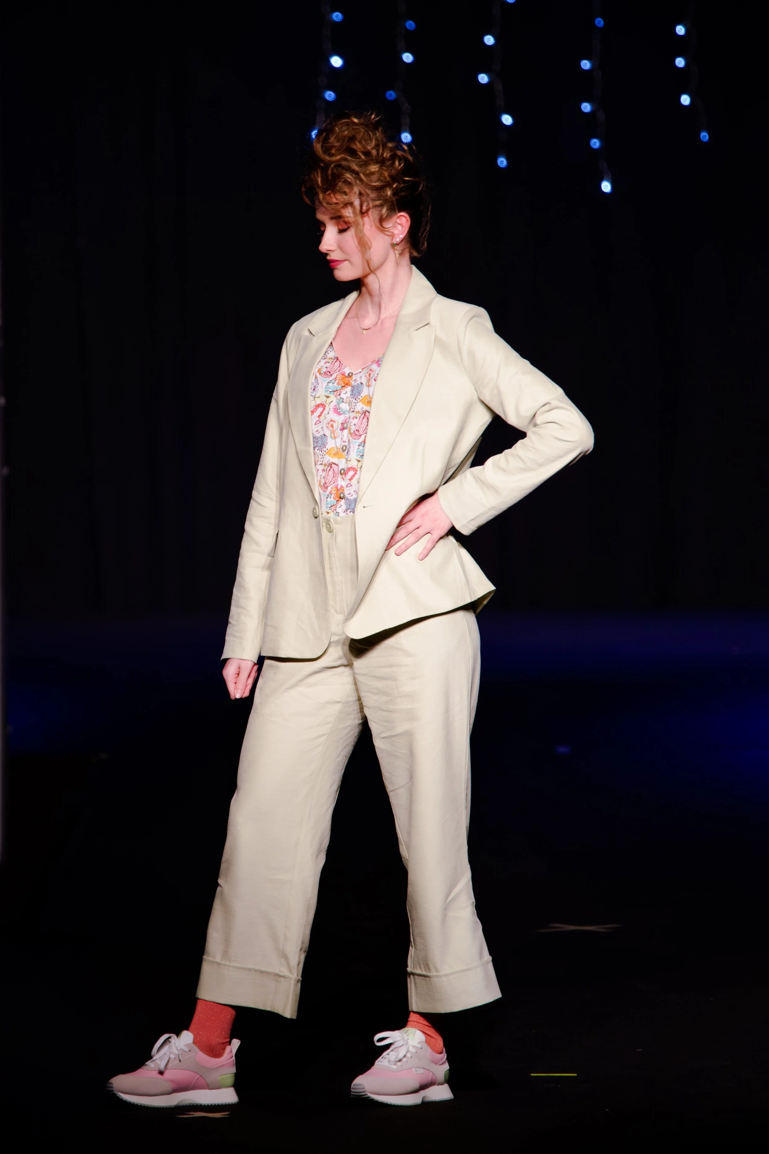 Mannequin portant un costume de couleur claire, un haut à motifs et des baskets sur un podium de mode avec un fond sombre.