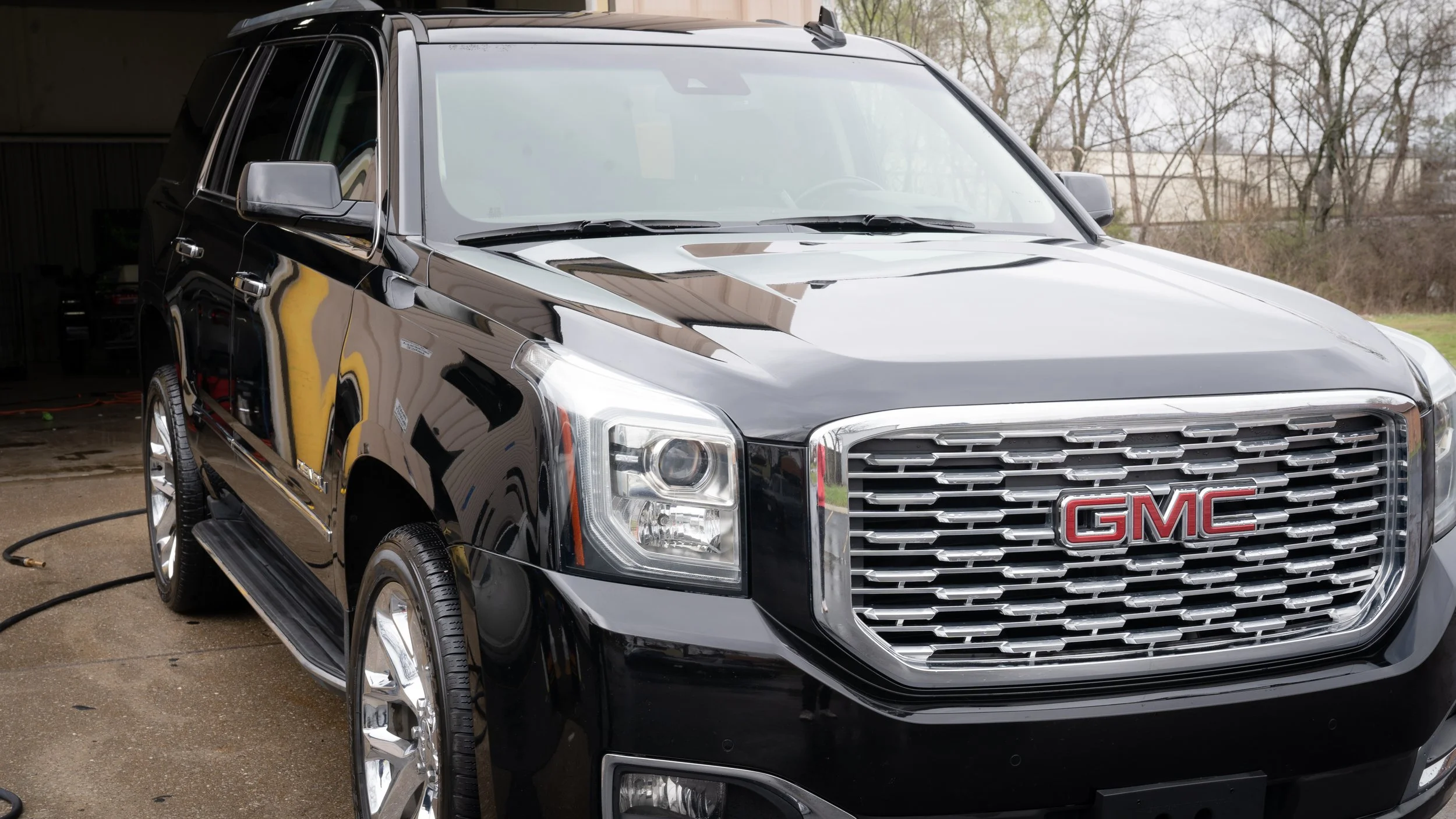 Black GMC SUV parked outdoors with a chrome grille, rectangular headlights, and chrome wheels.