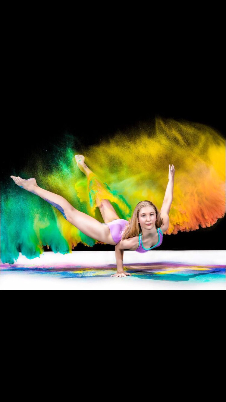 Sarah Childs balancing in a contortion pose in front of a burst of colored powder