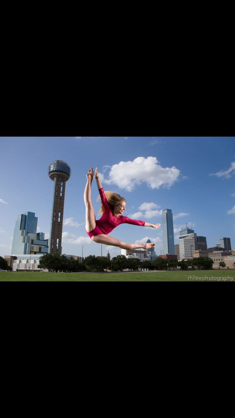 Sarah Childs in a split leap in front of the Dallas skyline