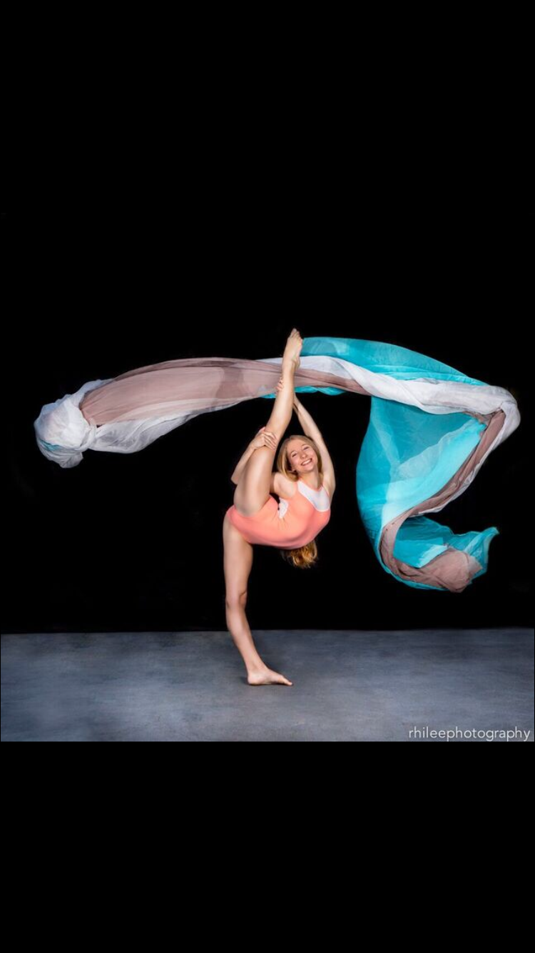 Sarah Childs in a standing leg hold with flowing teal and white fabric