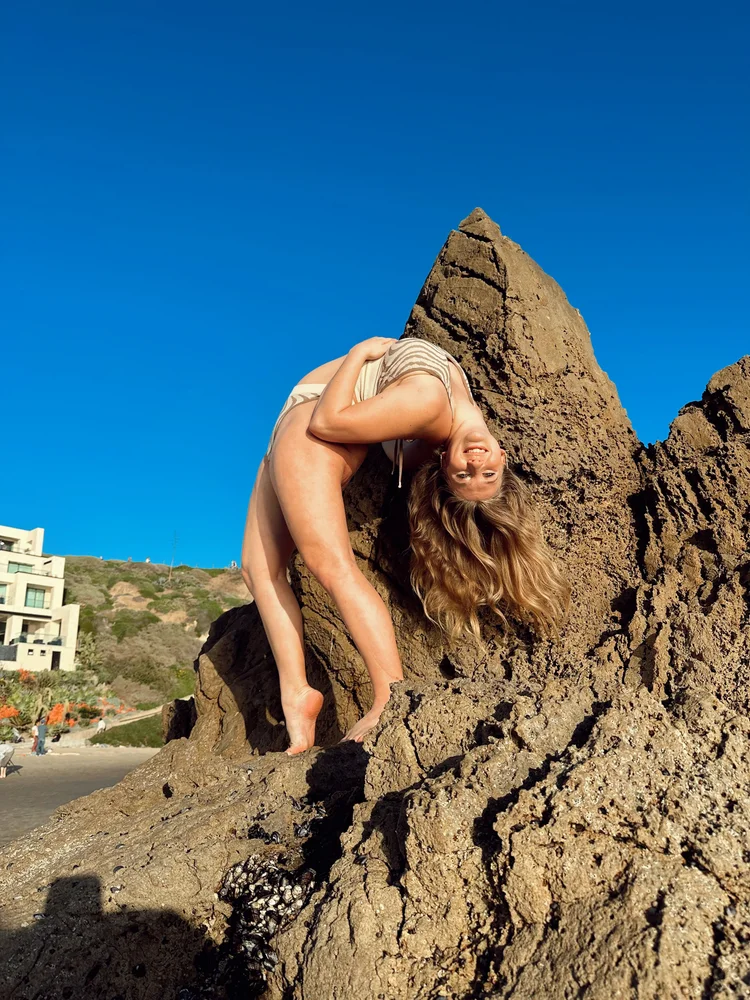 Sarah Childs in a standing backbend on a rocky outcrop by the ocean