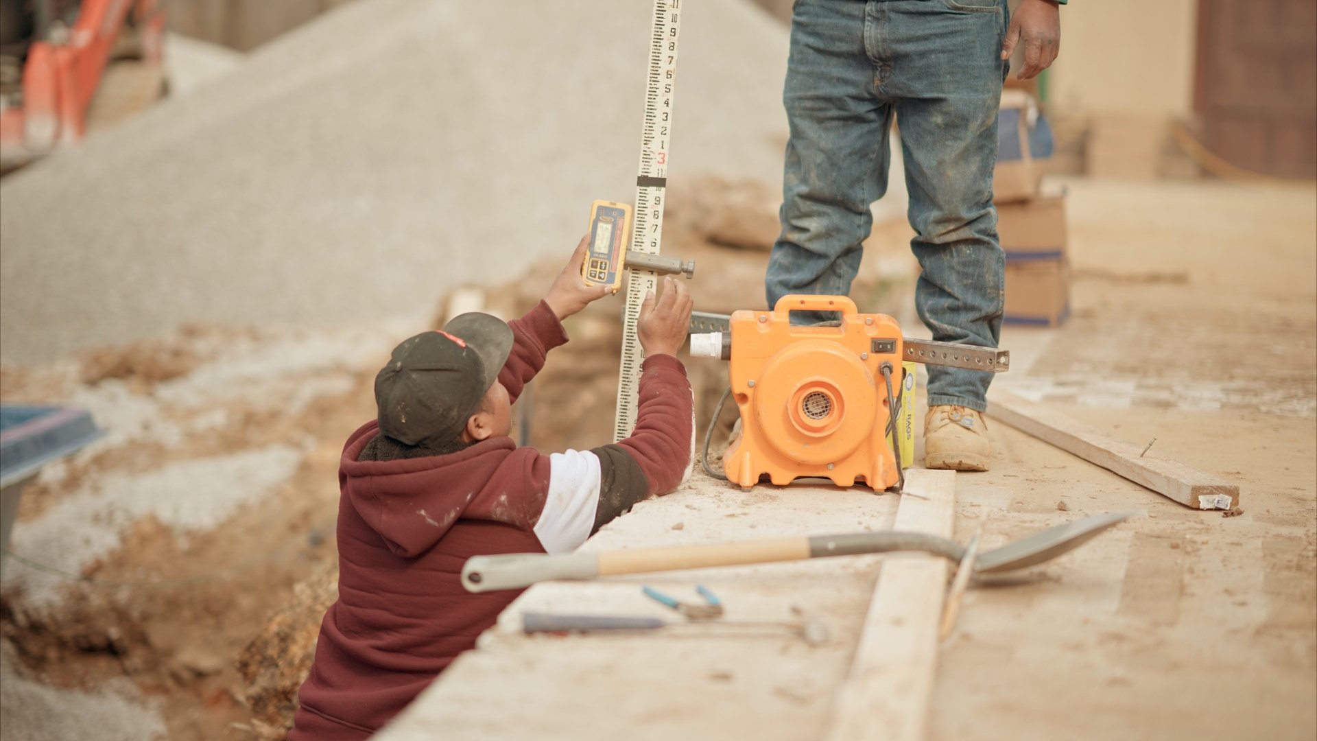 Construction workers using a leveling device and measuring tools on a building site.