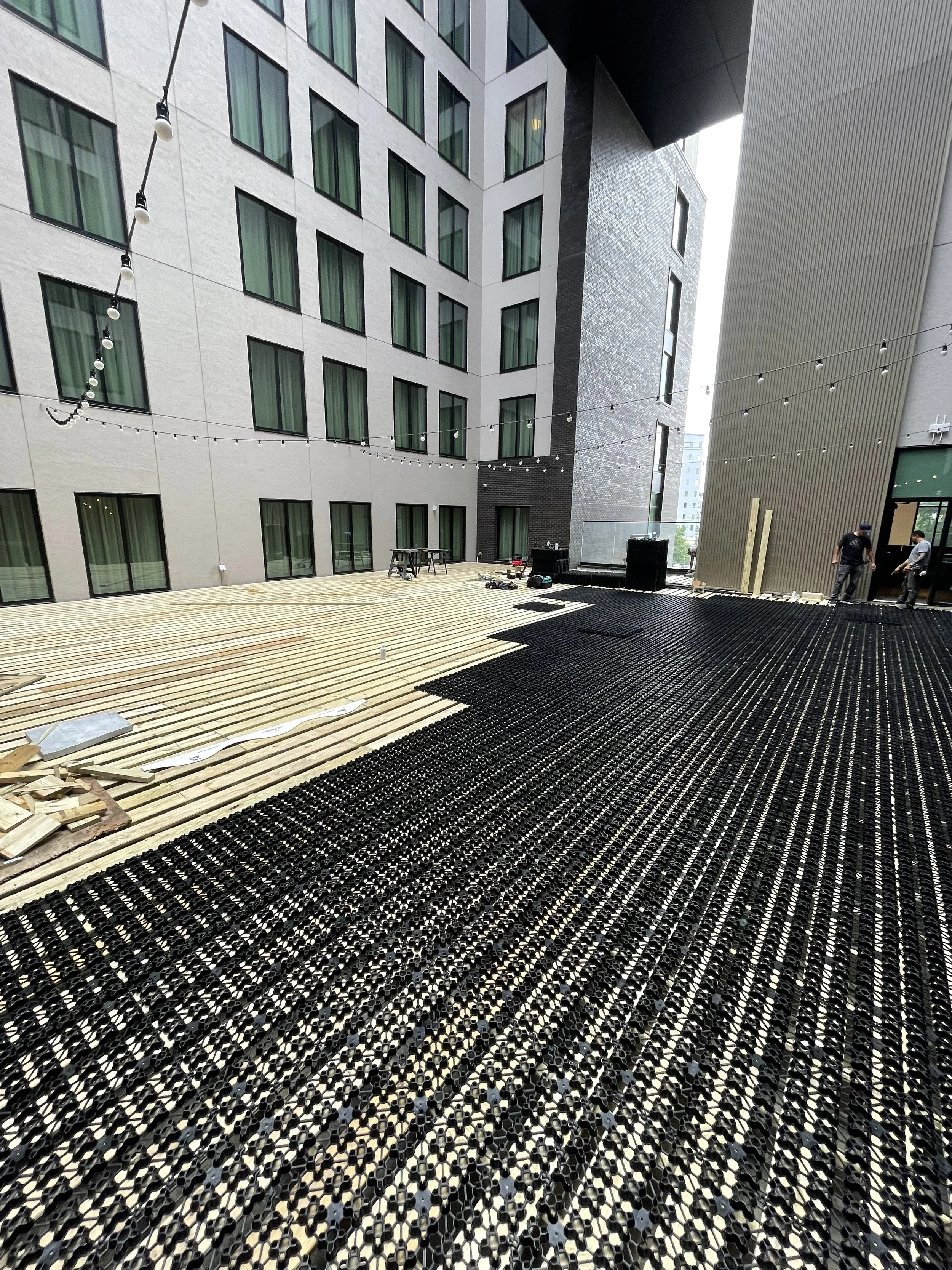 Building exterior with large windows, string lights, wooden deck, and construction materials on a rooftop.