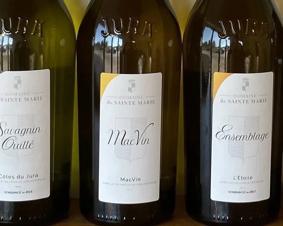 Trois bouteilles de vin de la domaine Sainte Marie avec des étiquettes indiquant Savagnin Oullé, Mac Vin, et Ensemblage, parmi d'autres détails.