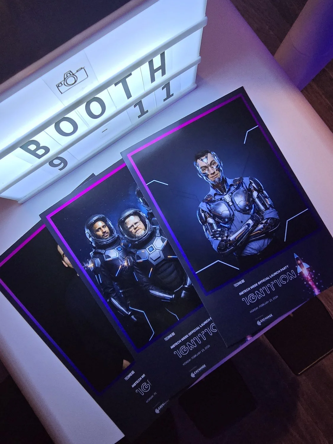 Printed AI portraits from a Winnipeg tech launch party fanned out beside the venue's booth sign, each carrying the event branding and sponsor logo