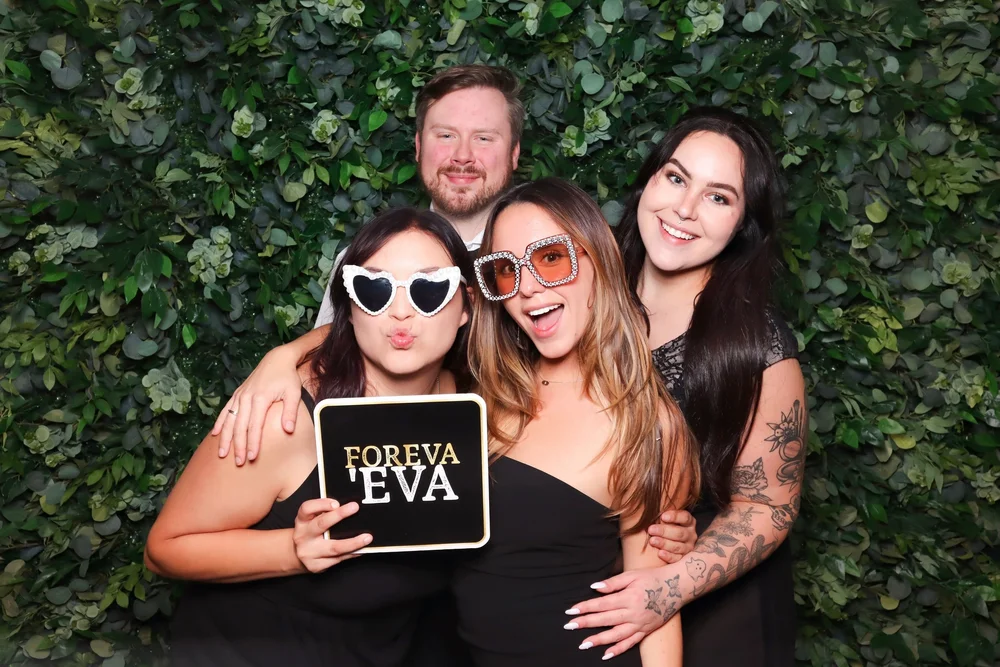 Friends with a sign in front of the greenery wall
