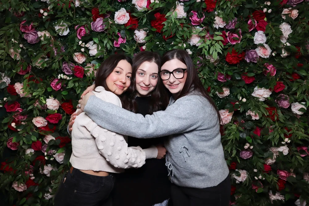 Two friends laughing in front of the Secret Garden flower wall