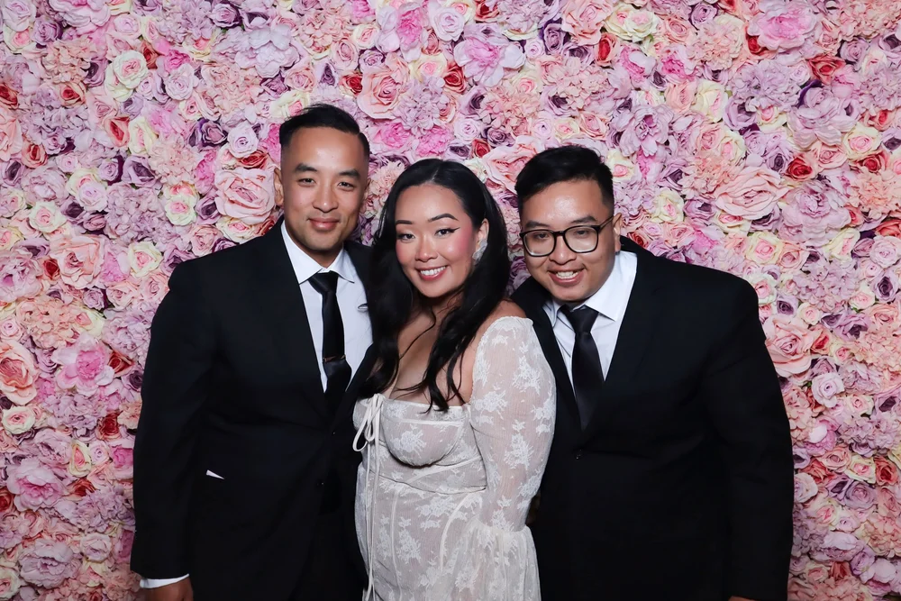 Guests in suits in front of the Pastel Dreams flower wall