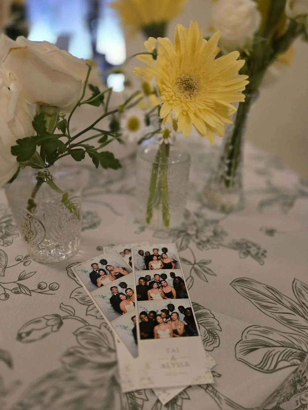 Classic photo strips from Tai and Alyssa's wedding on a floral tablecloth beside yellow flowers