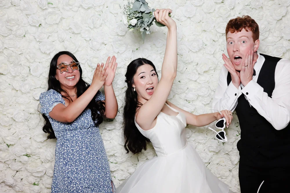 A bride and guests in front of the Rose Blanc flower wall at a Winnipeg wedding