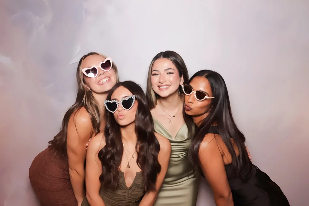 Four friends in heart sunglasses posing at an On Que photo booth in Winnipeg