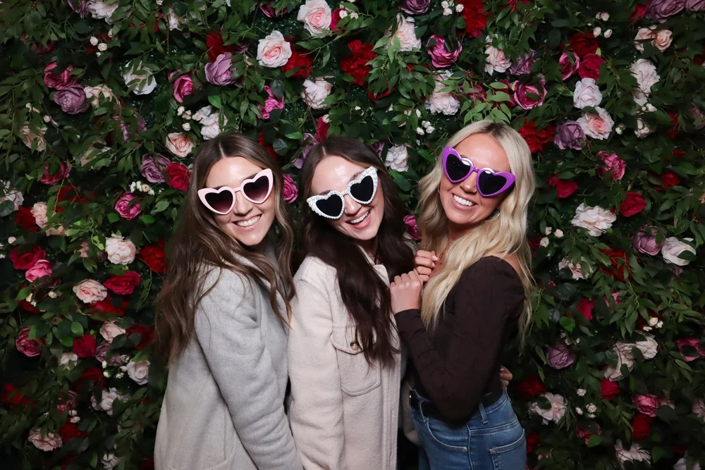 Two guests in sunglasses in front of the Secret Garden flower wall