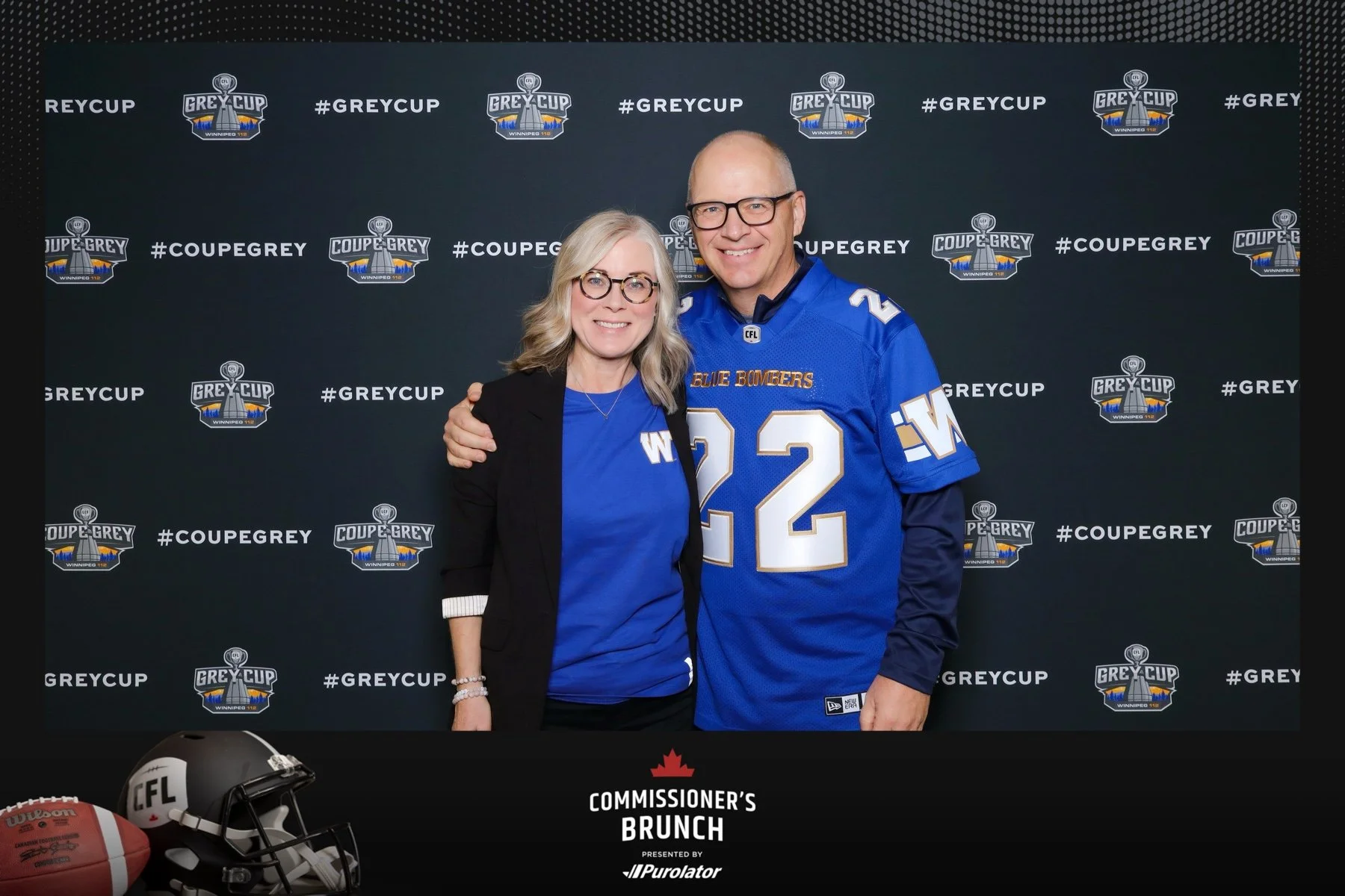 a couple wearing Winnipeg Blue Bombers jerseys posing on a Grey Cup branded background
