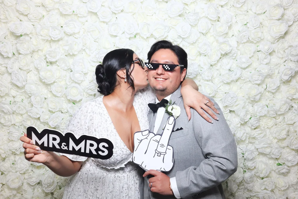A couple holding a Mr and Mrs sign in front of the white rose flower wall