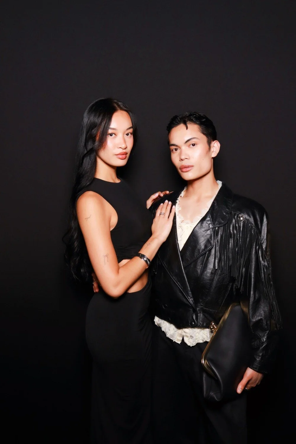 A couple dressed in black posing for a glam portrait on a black backdrop