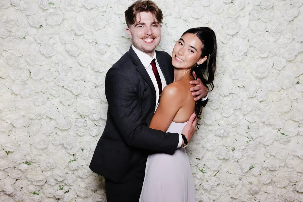 A couple in front of the white rose flower wall at a wedding