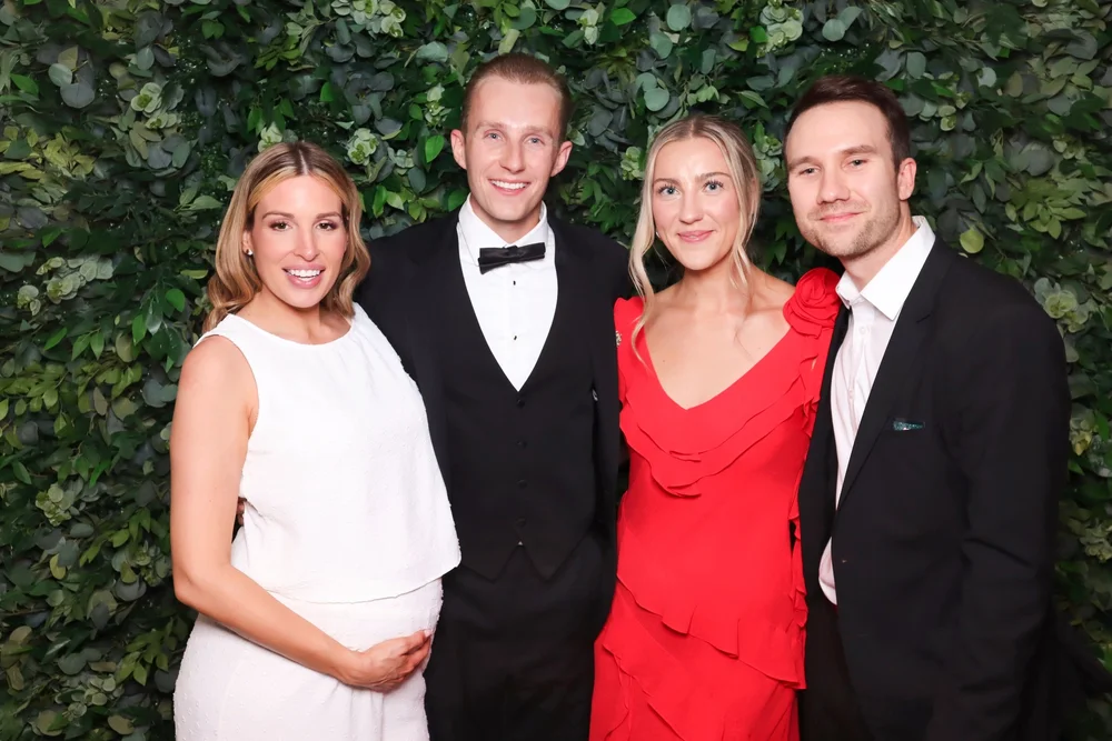 Four guests dressed up in front of the greenery wall