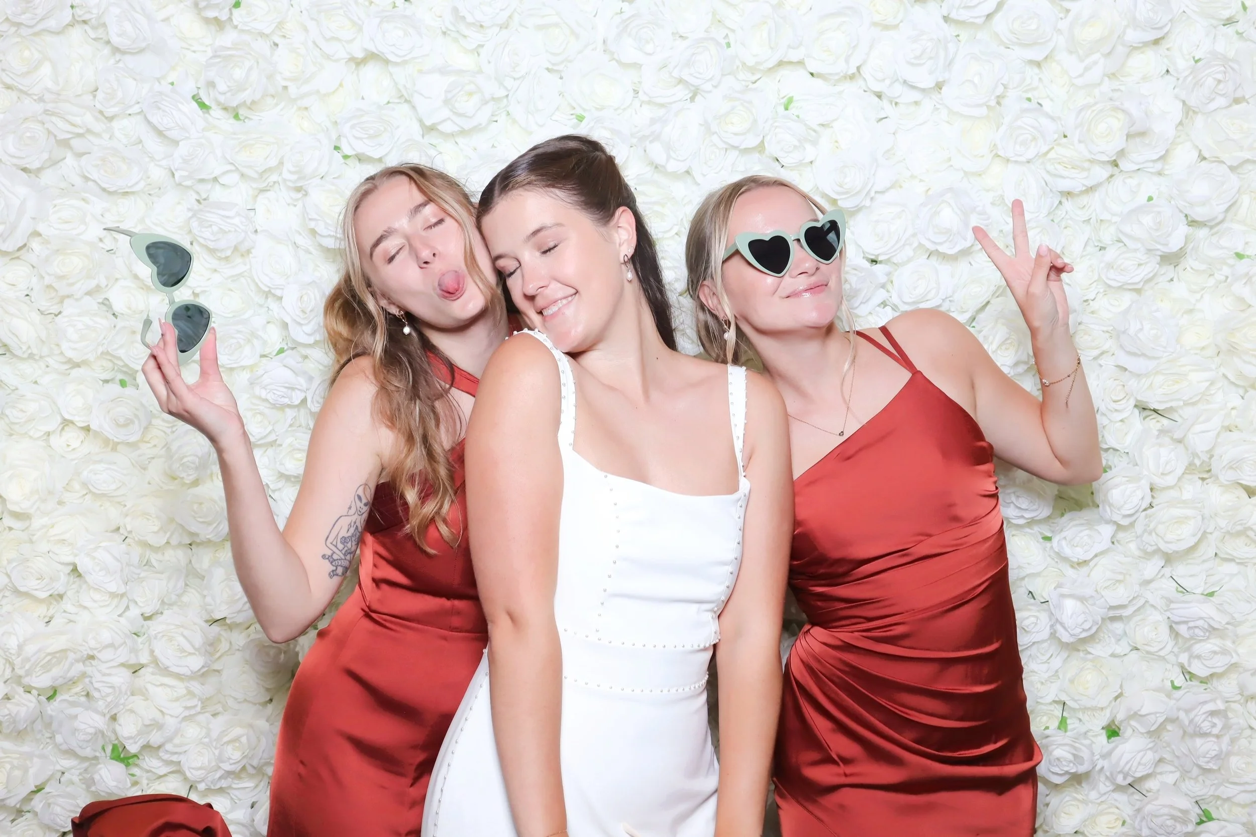 A bride posng with two bridesmaids on a white floral backdrop