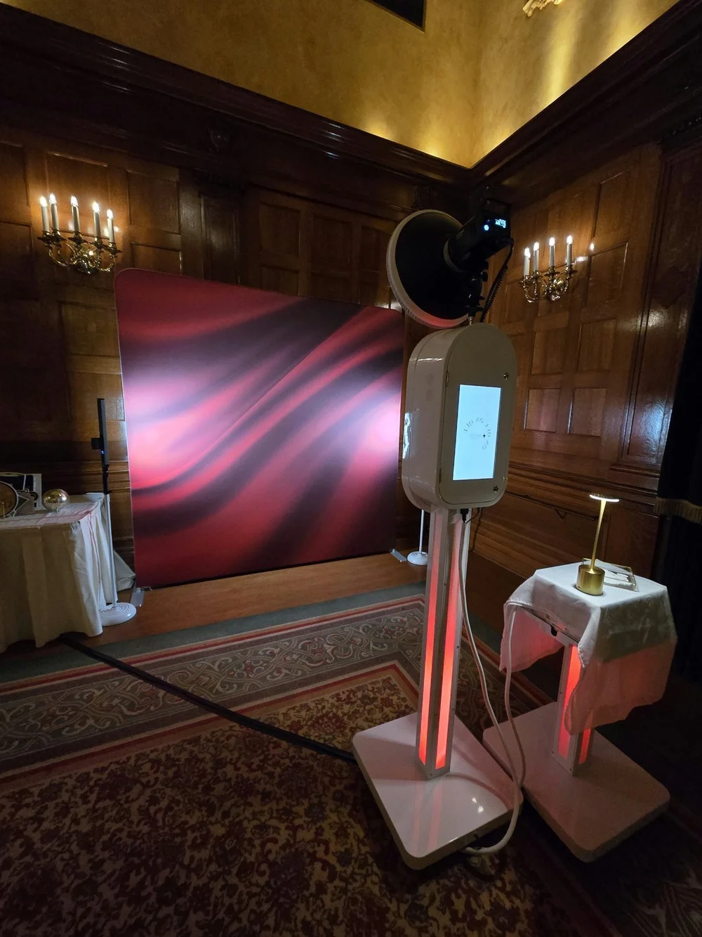 The Aura booth, column lit red, in front of a deep red backdrop in a wood panelled Winnipeg ballroom