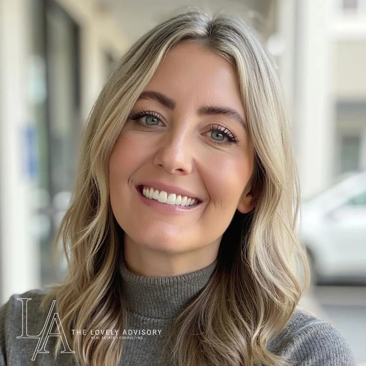 Close-up of a smiling woman with blonde hair and blue eyes, wearing a gray turtleneck, in an urban setting.