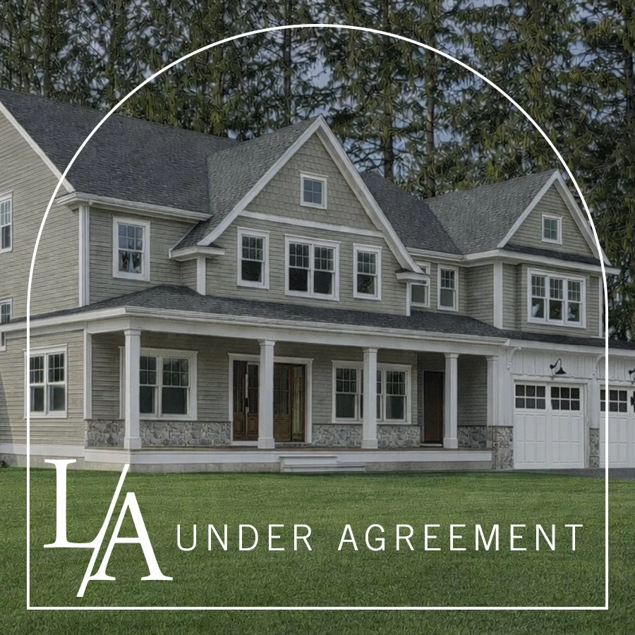 A large, multi-story house with a gray exterior and a front porch, surrounded by green grass and trees in the background, with a white overlay and the words "LA Under Agreement" indicating the house is under contract.