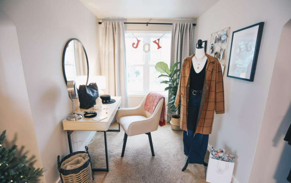 Bedroom sitting area with simple desk and chair with a clothing manequin wearing a tweed coat and belted dress.png