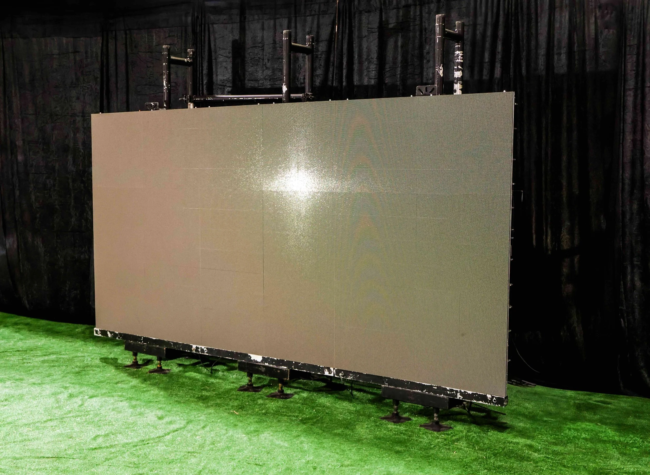 A large LED screen on a stand, set up on a green carpet, with a black curtain in the background.