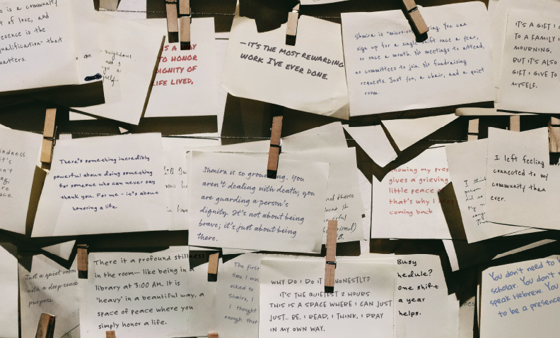 Image of a lot of index cards hanging on line with clothespins - each card has a handwritten note about why a volunteer sits shmira