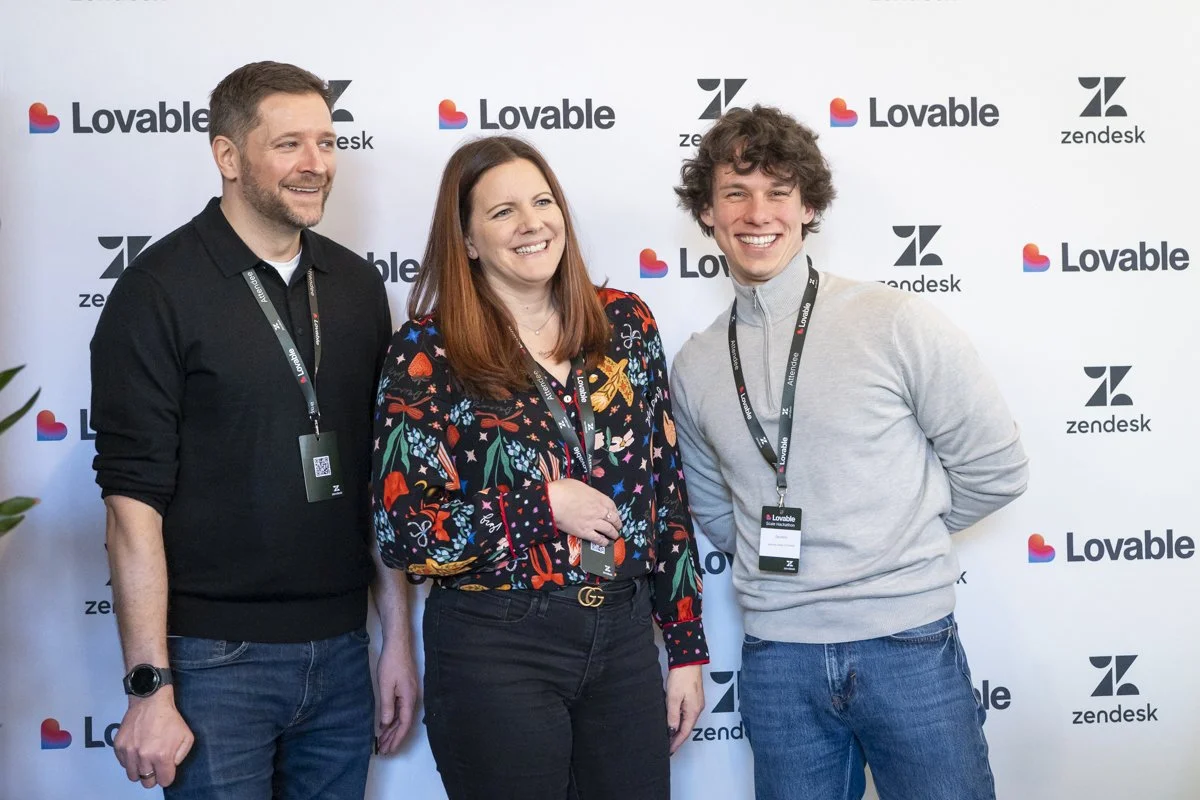 Three people smile and pose for a photo at a Zendesk and Lovable event, standing in front of a step-and-repeat backdrop with the logos of Zendesk and Lovable.