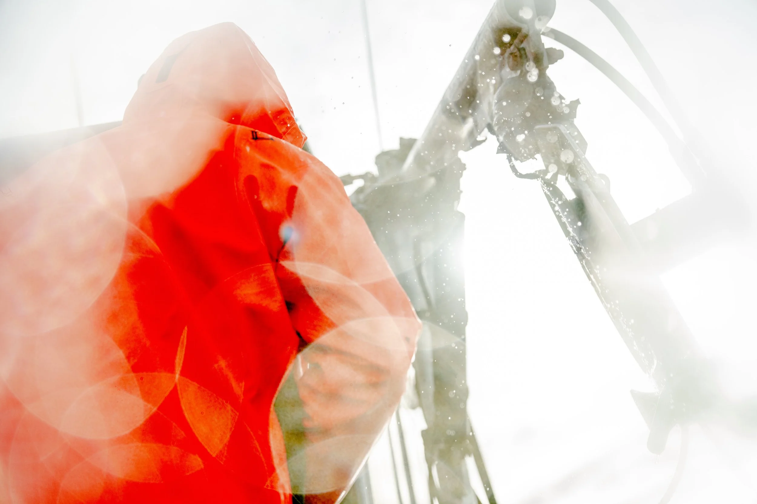 A person wearing an orange jacket and hood with water splashing around them.