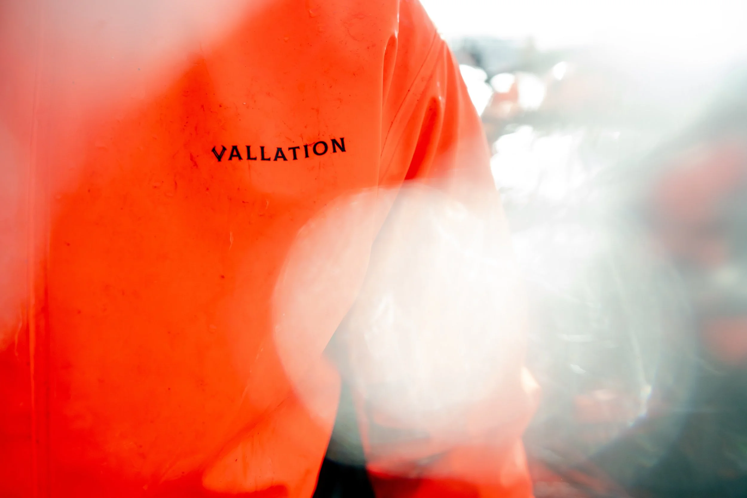 Close-up of an orange jacket with the word 'VALLATION' printed on it, out of focus with bright light and blurred background.
