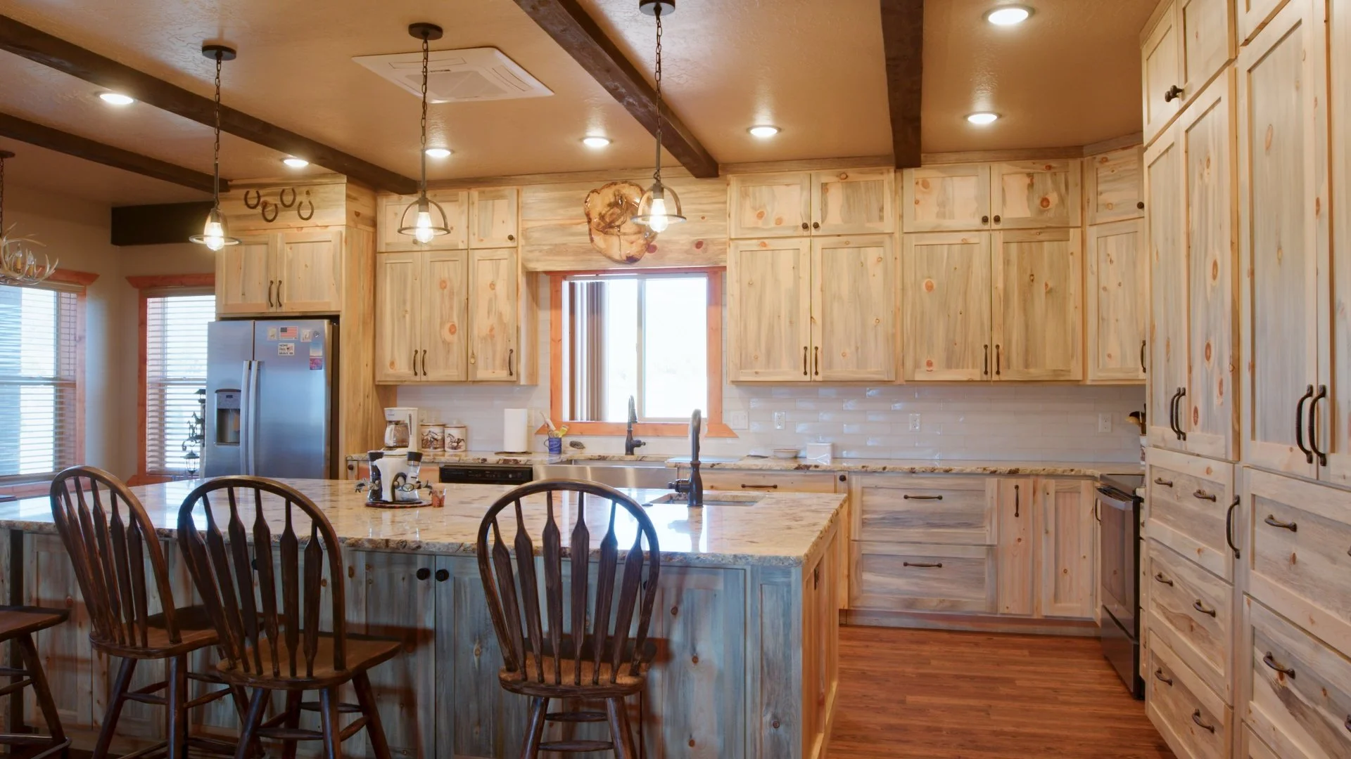 Kitchen with light wood cabinets, granite countertops, a kitchen island with stools, stainless steel refrigerator, and a window above the sink.