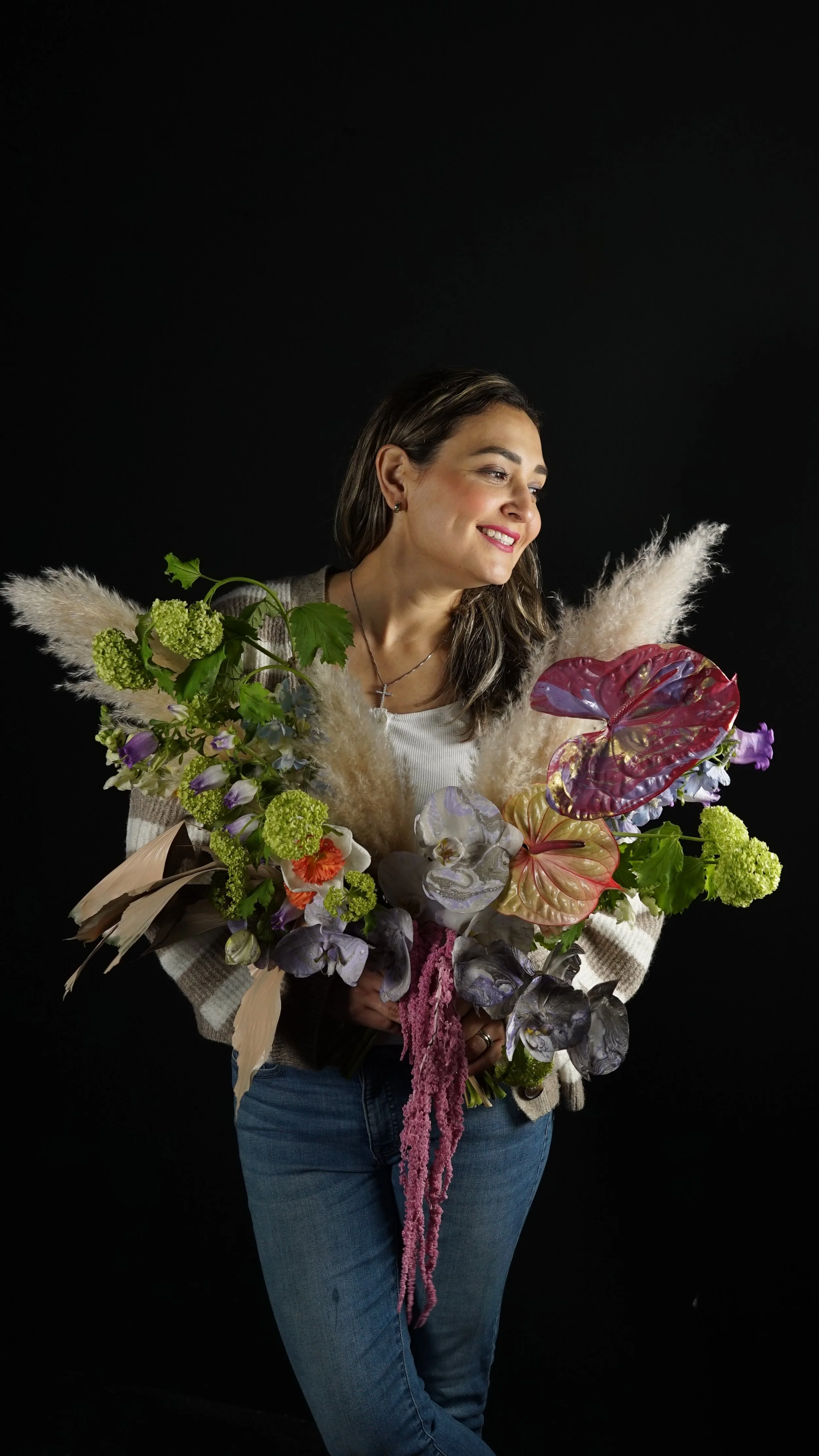 Mujer sonriendo sosteniendo un ramo de flores coloridas y variadas, con fondo negro.