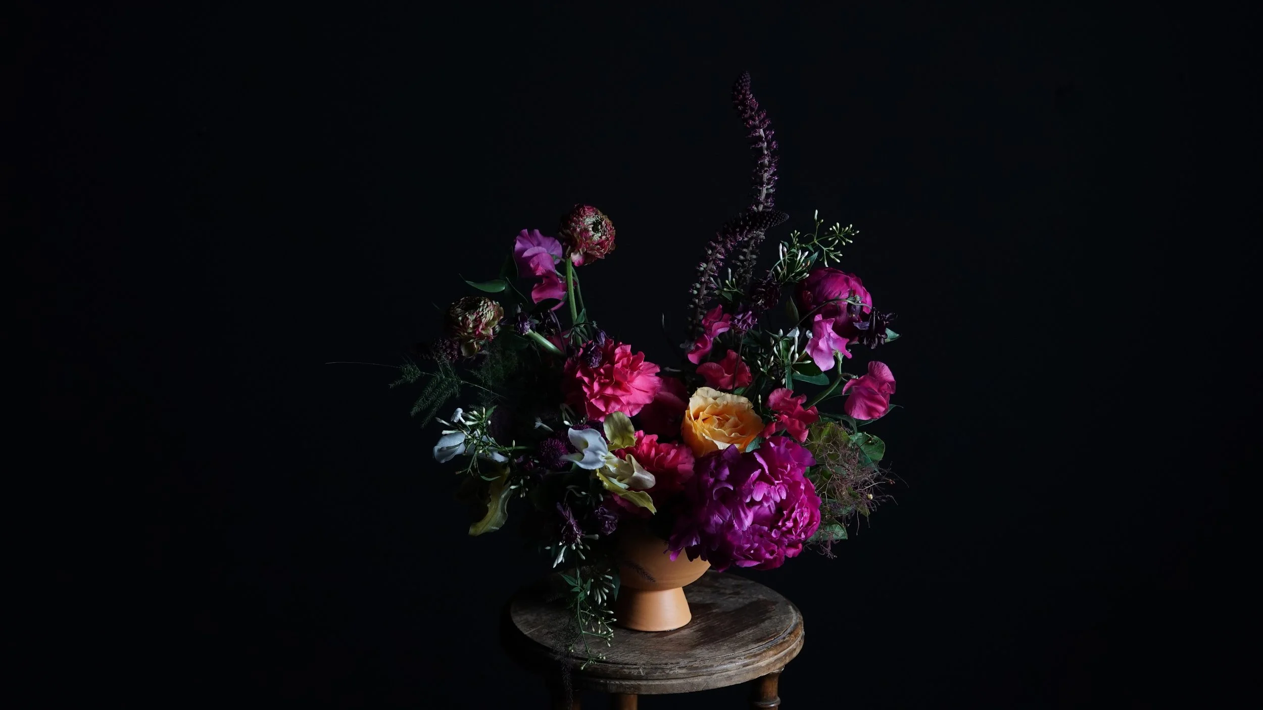 Ramo de flores de colores en jarrón en un fondo negro, colocado sobre una mesa de madera.