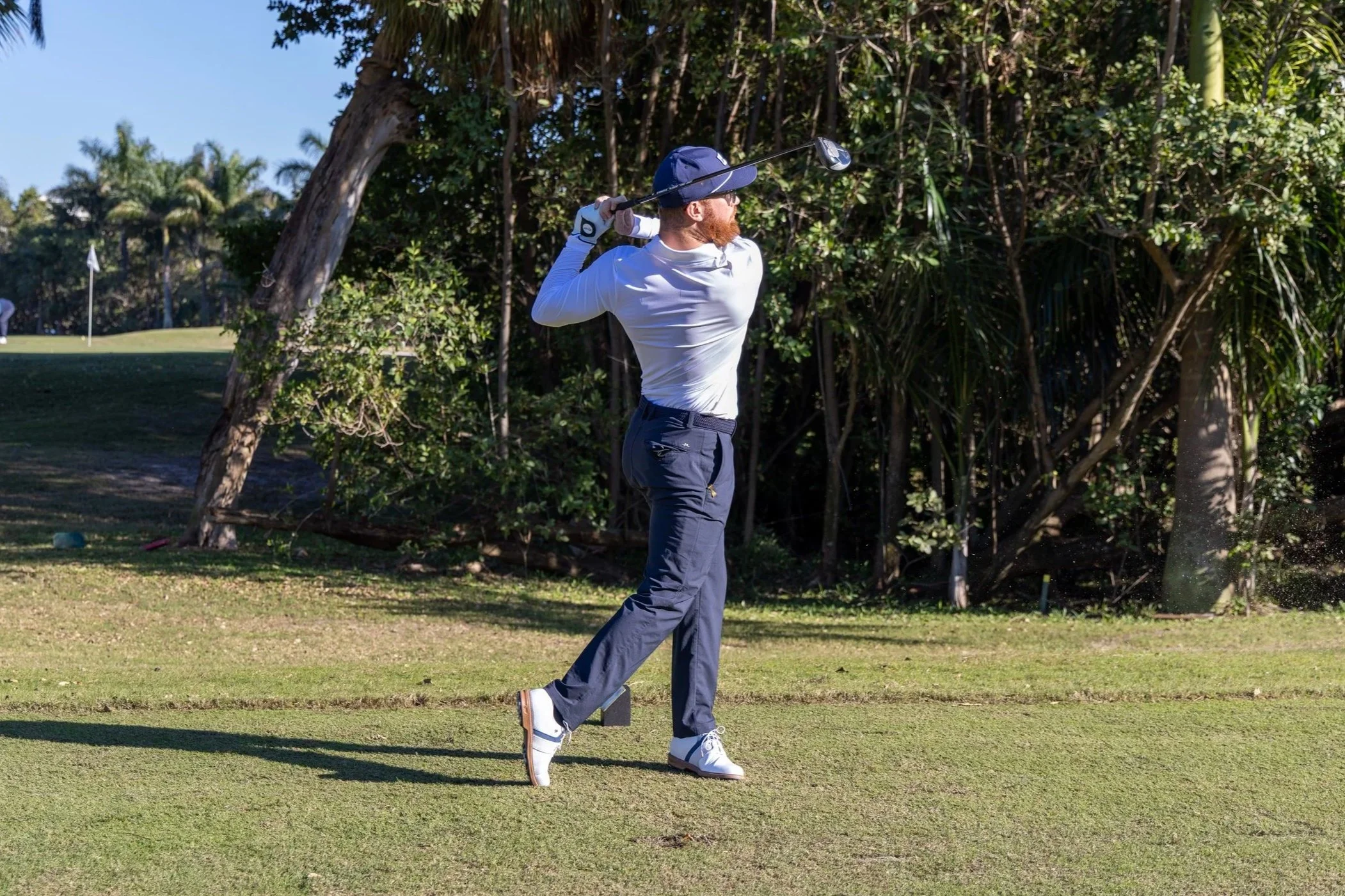 A man playing golf on a lush green course with trees in the background, swinging a golf club.