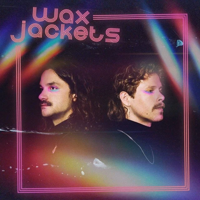 Album cover of Wax Jackets featuring two men with curly hair and mustaches, neon makeup, and dark clothing, with a rainbow-colored light streak and pink neon border.