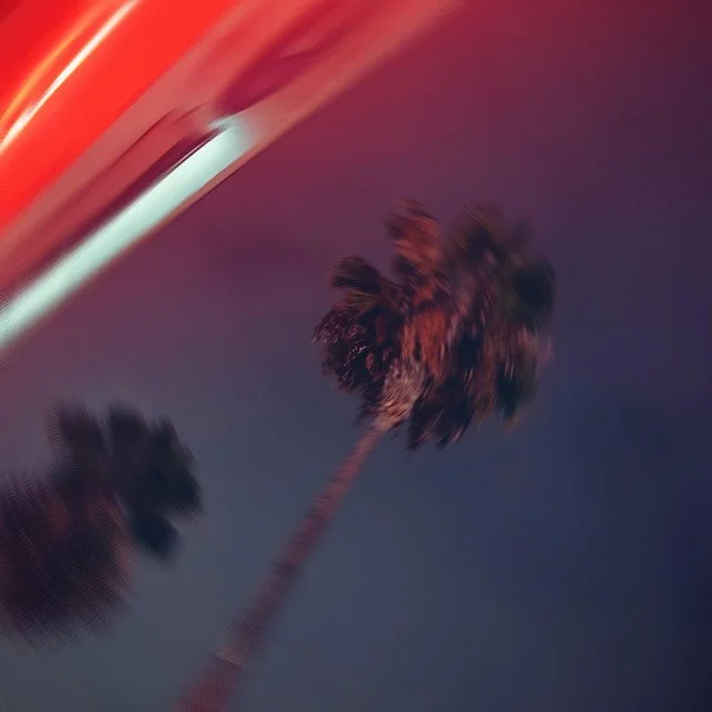 Blurred image of palm trees against a colorful sky with red and purple hues.