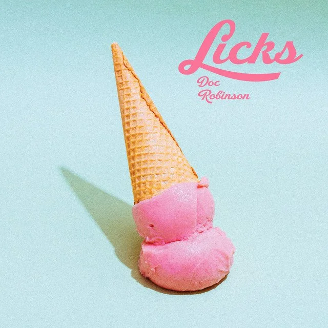 A pink ice cream cone with three scoops, laying on a light teal background. The cone is upside down, with the scoops at the bottom. The word 'Licks' in pink cursive is in the upper right corner, with 'Doc Robinson' written below it.