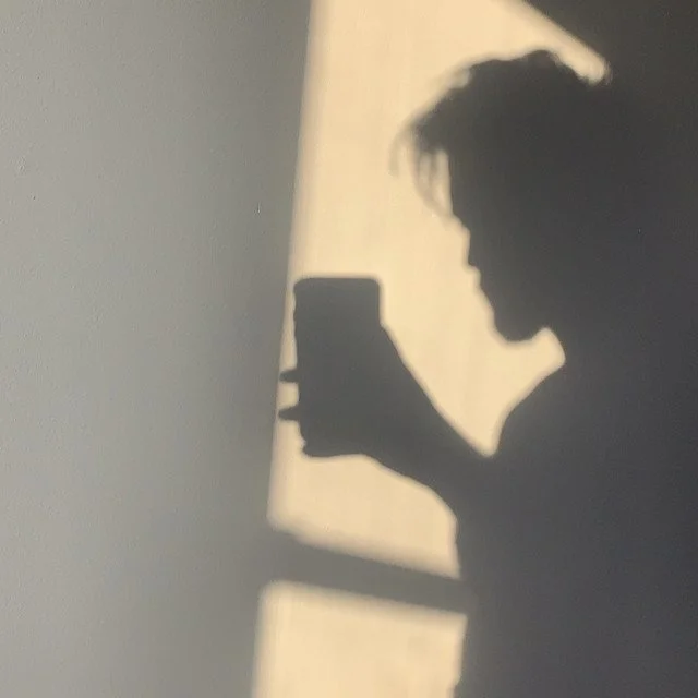 Silhouette of a person taking a selfie with a smartphone, cast in shadow on a wall.