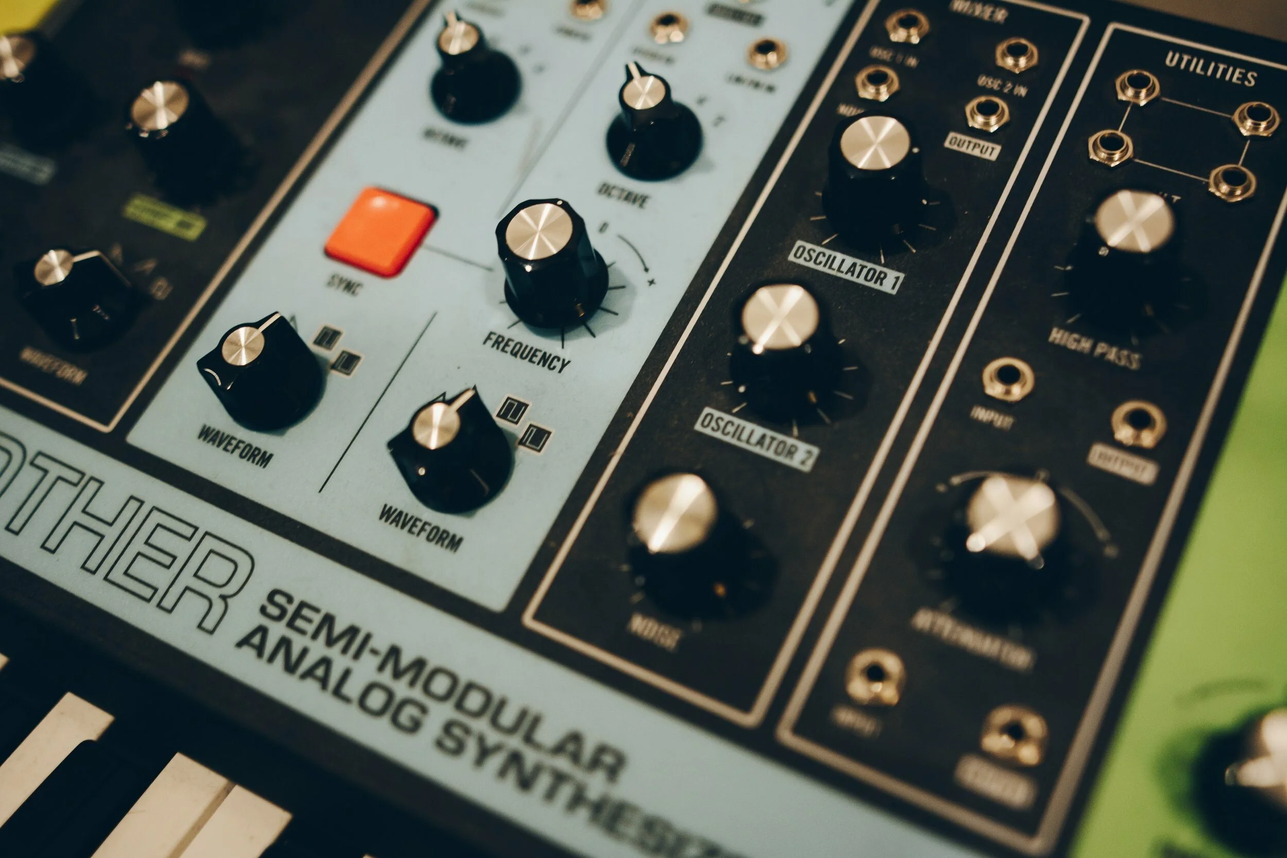 Close-up of a modular synthesizer with various black and brass control knobs, switches, and patch points, with part of a keyboard visible at the bottom.