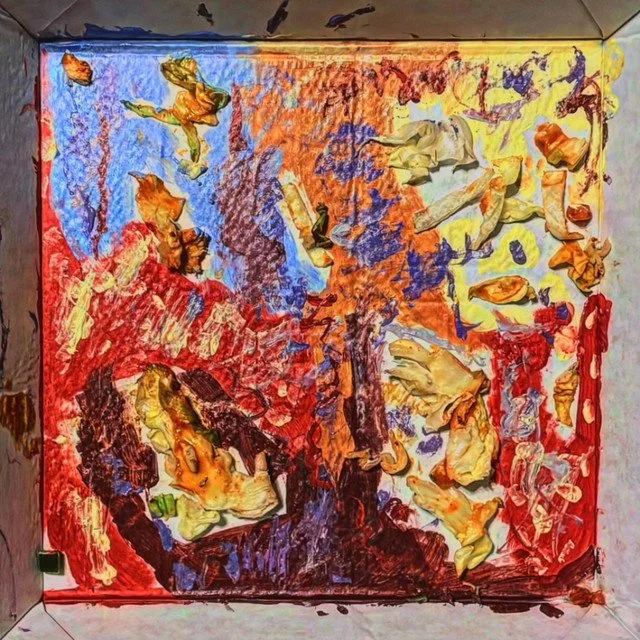 Abstract painting with vibrant swirls of red, orange, yellow, blue, purple, and black, featuring textured areas of yellow and beige. The painting is in an open box frame, resembling an expressive, textured artwork.