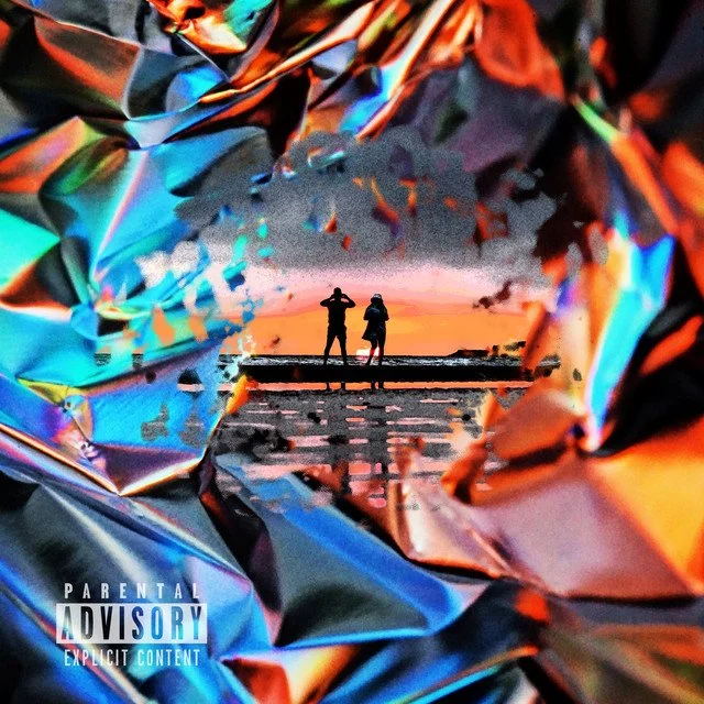 Two people walking along a beach during sunset, viewed through a hole in shiny, crinkled metallic foil.