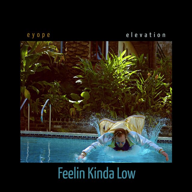 Person in a yellow raincoat diving into a swimming pool surrounded by greenery.