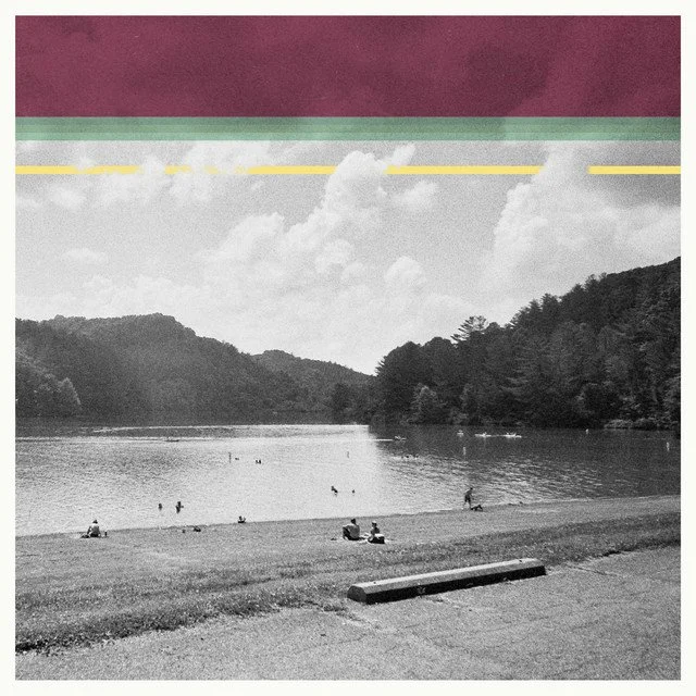 A black and white photo of a lakeside scene with a few people sitting and walking on the beach, surrounded by tree-covered hills, with the sky partly cloudy, and a colorful abstract strip at the top of the image.