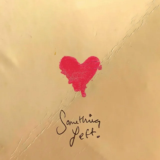 A red heart drawn on a light beige paper with a message that reads 'Something left' written below it.