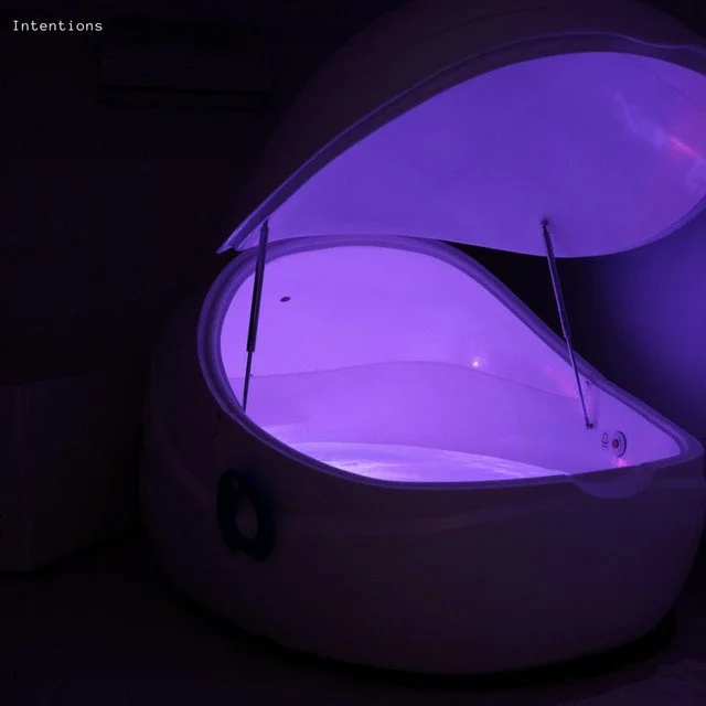 A futuristic pod-shaped tanning bed illuminated with purple light in a dark room.