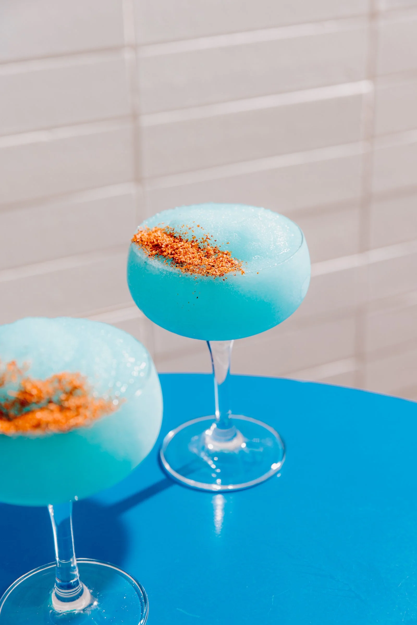 Two blue frozen cocktails in coupe glasses on a bright blue table at Good Heavens Rooftop Bar